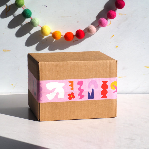 An image of a box sealed with cute pink tape with abstract patterns and pompoms in the background.